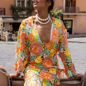 Donna con copricostume floreale ricamato dai toni caldi seduta su una 500 decorata in stile siciliano, in una piazza mediterranea.