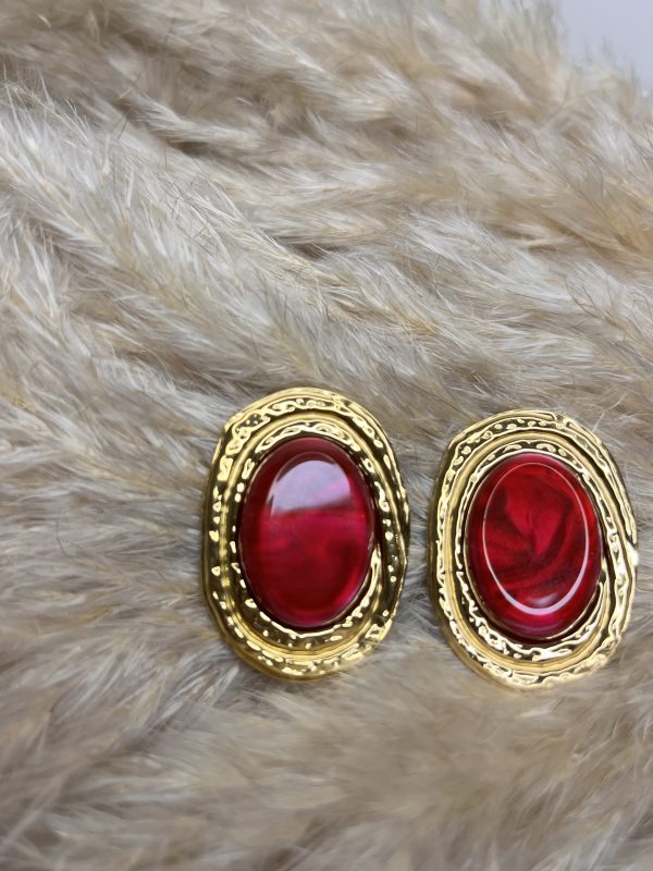 Orecchini ovali con cabochon rosso intenso e cornice dorata martellata, dal carattere elegante e deciso.