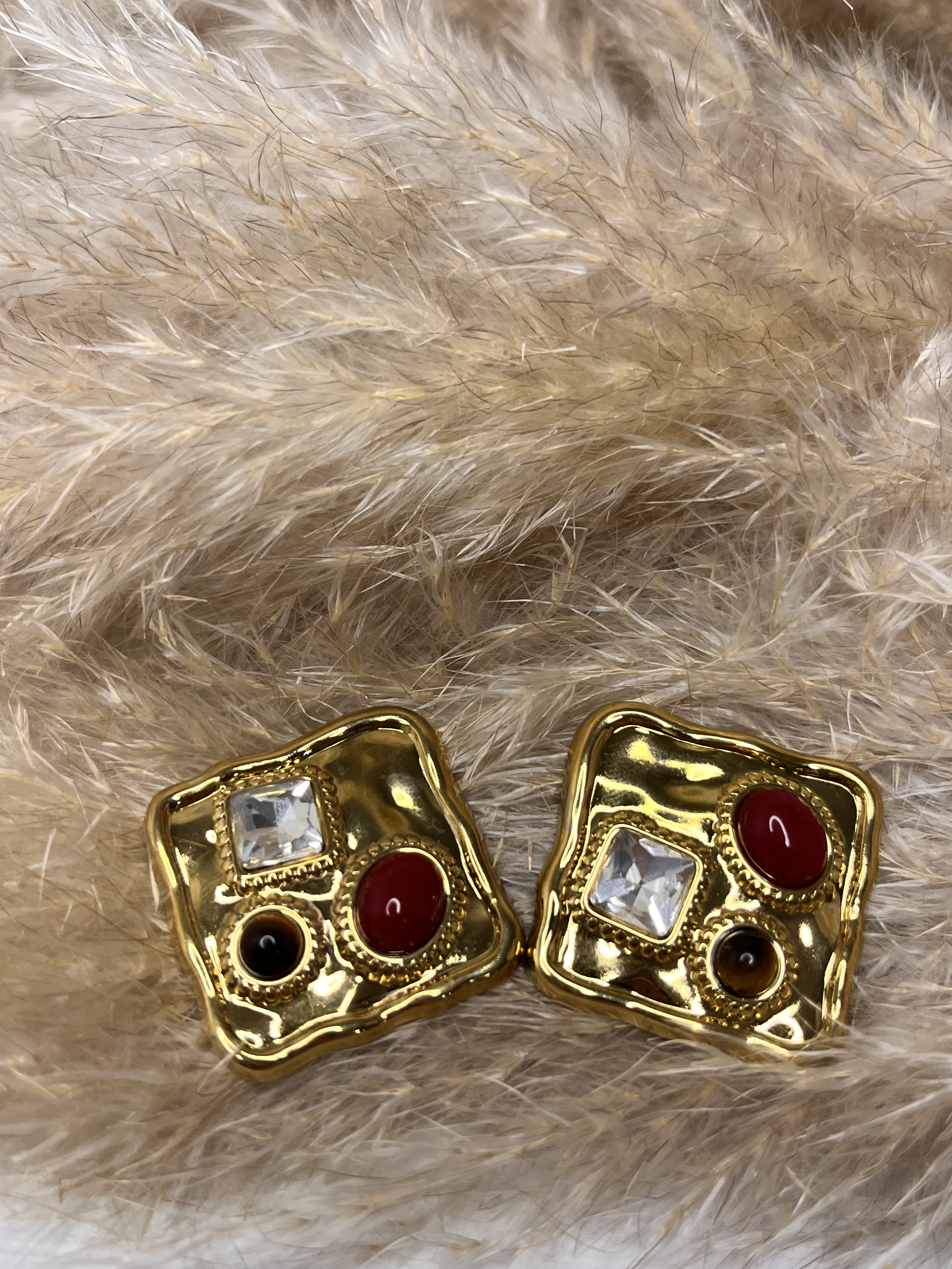 Orecchini dorati dal design artistico con gemme rosse, nere e cristallo trasparente. Un mix di forme e colori che cattura lo sguardo.