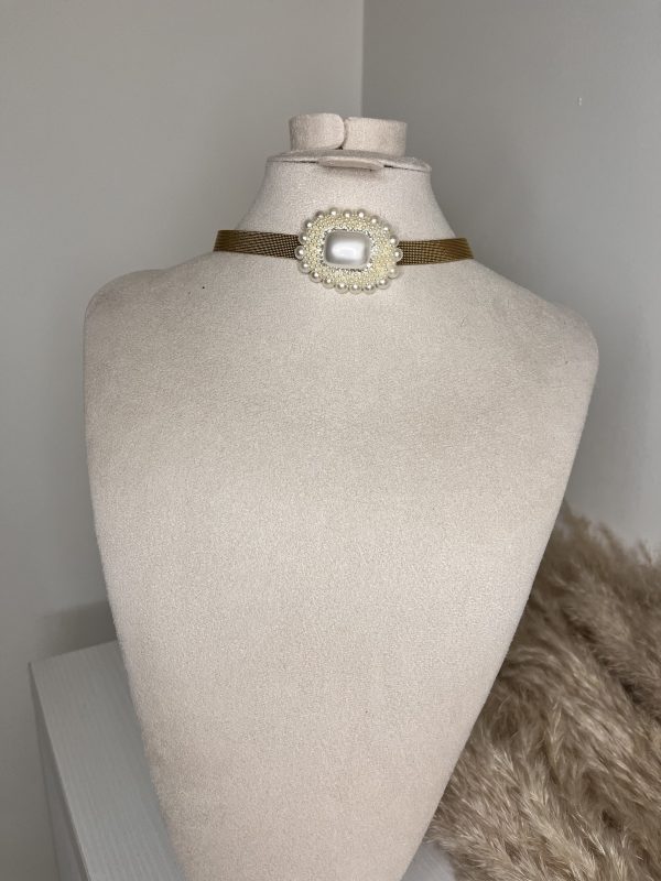 Un gioiello da vera Regina! Questo choker Elisabeth Fashion presenta un'elegante fascia color oro antico e un medaglione centrale con gemma rettangolare effetto madreperla, circondata da un pavé di piccole perle. Un accessorio regale e sofisticato, perfetto per un total look Diva elegante e d'impatto.
