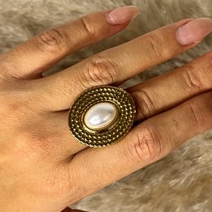 Un anello statement che evoca il lusso retrò! Questo anello Elisabeth Fashion presenta una grande montatura oro lucido con una texture lavorata che incornicia una gemma ovale effetto madreperla/perla. Perfetto per un tocco glamour audace e un'eleganza senza tempo.