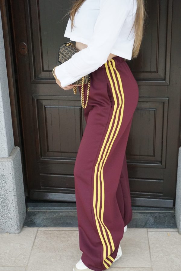 Pantaloni granata intenso a gamba larga con bande laterali gialle. Comodi, moderni e dal forte impatto visivo: perfetti per look sporty-street di carattere.